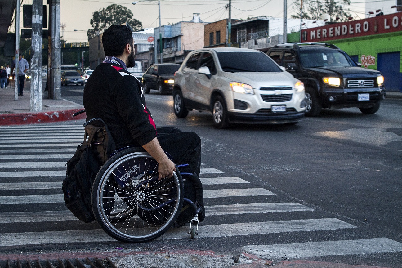 Un hombre en silla de ruedas espera su oportunidad de cruzar una calle en la Ciudad de Guatemala.