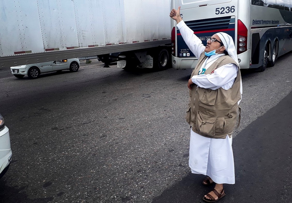 Una religiosa y un policía pidiendo aventón para los migrantes